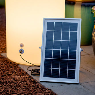 Solar Panel Charger for LED Garden & Pathway Lights on patio, powering a glowing cylindrical lamp, showcasing its off-grid capability for sustainable outdoor lighting.