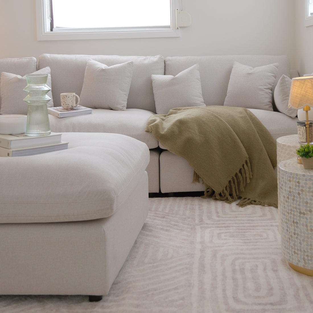 Light beige sectional sofa in a bright modern living room with pillows and blanket
