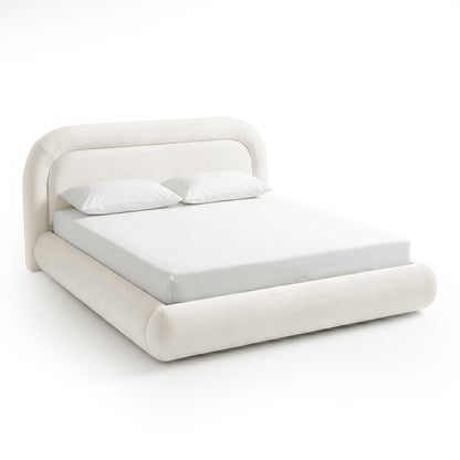 Three-quarter view of a complete ivory upholstered bed with mattress and pillows on a white background