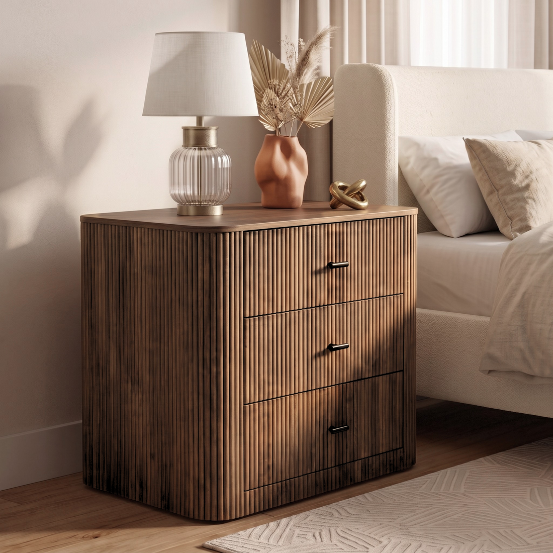 Wooden three-drawer nightstand styled beside a bed in a bedroom