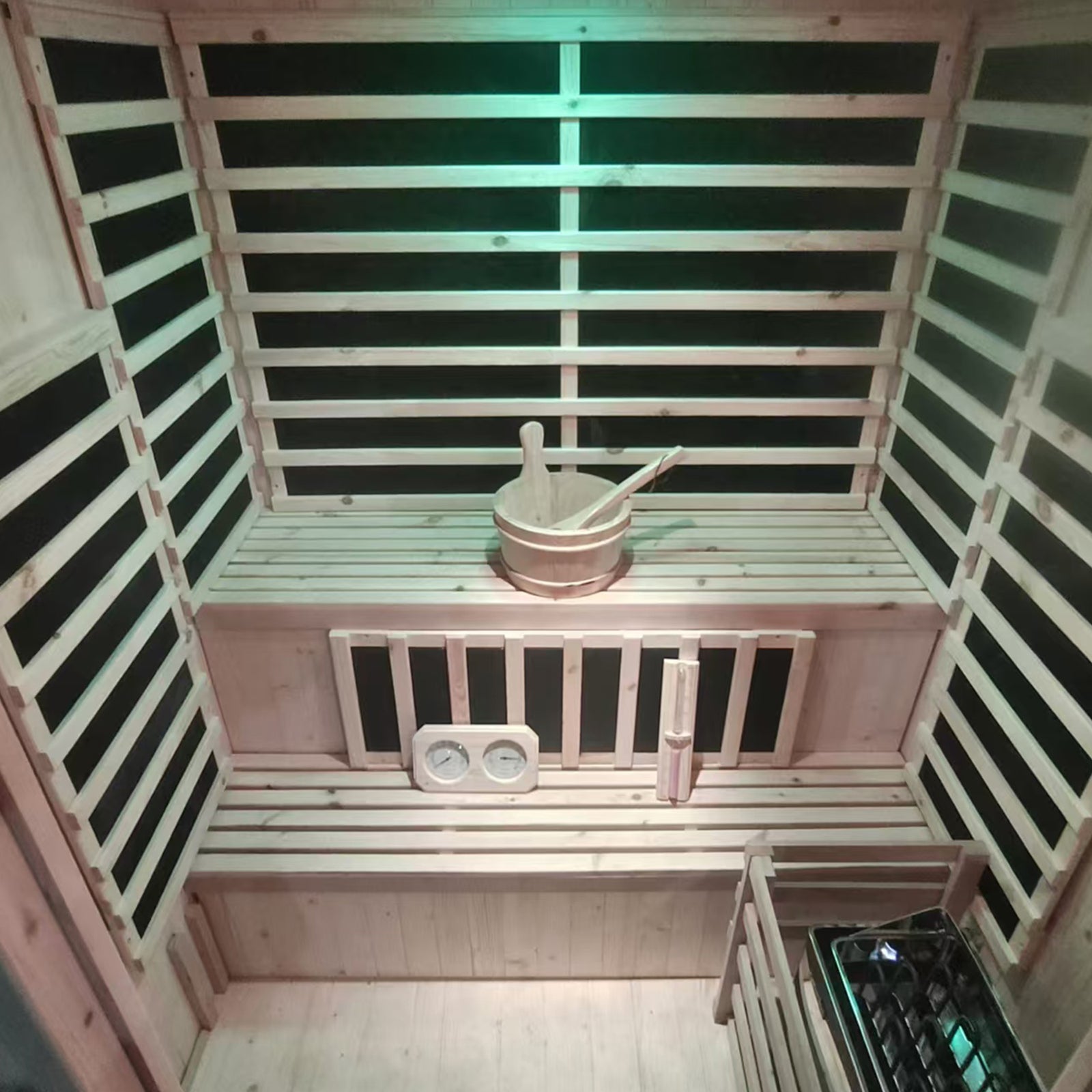 Luxo Kiima 3 Person Hybrid Finnish Outdoor Sauna in Natural features two-tier slatted wood benches, a sauna bucket with ladle, thermometer/hygrometer, hourglass, and a traditional sauna heater with stones.