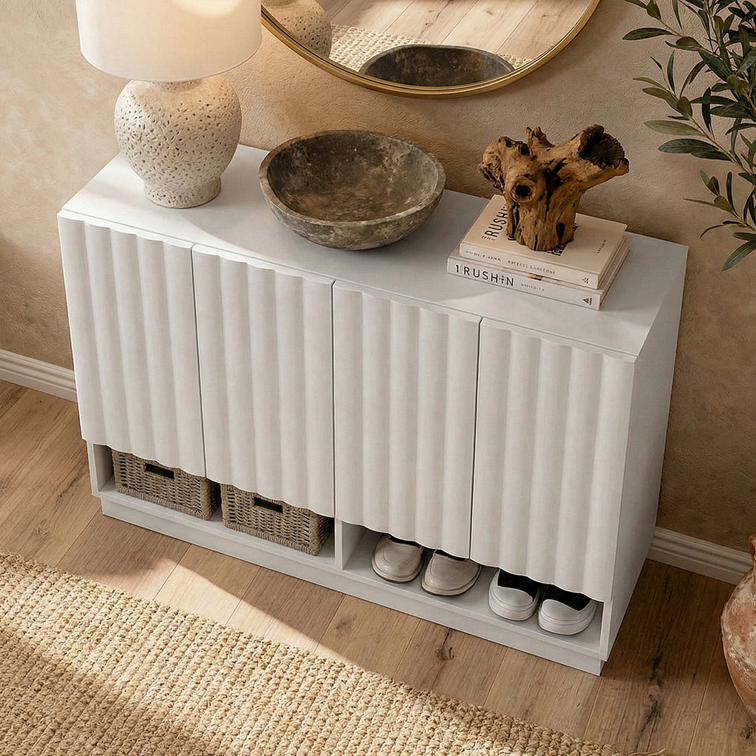 White console cabinet styled in room with lamp, bowl, books, driftwood, round mirror above