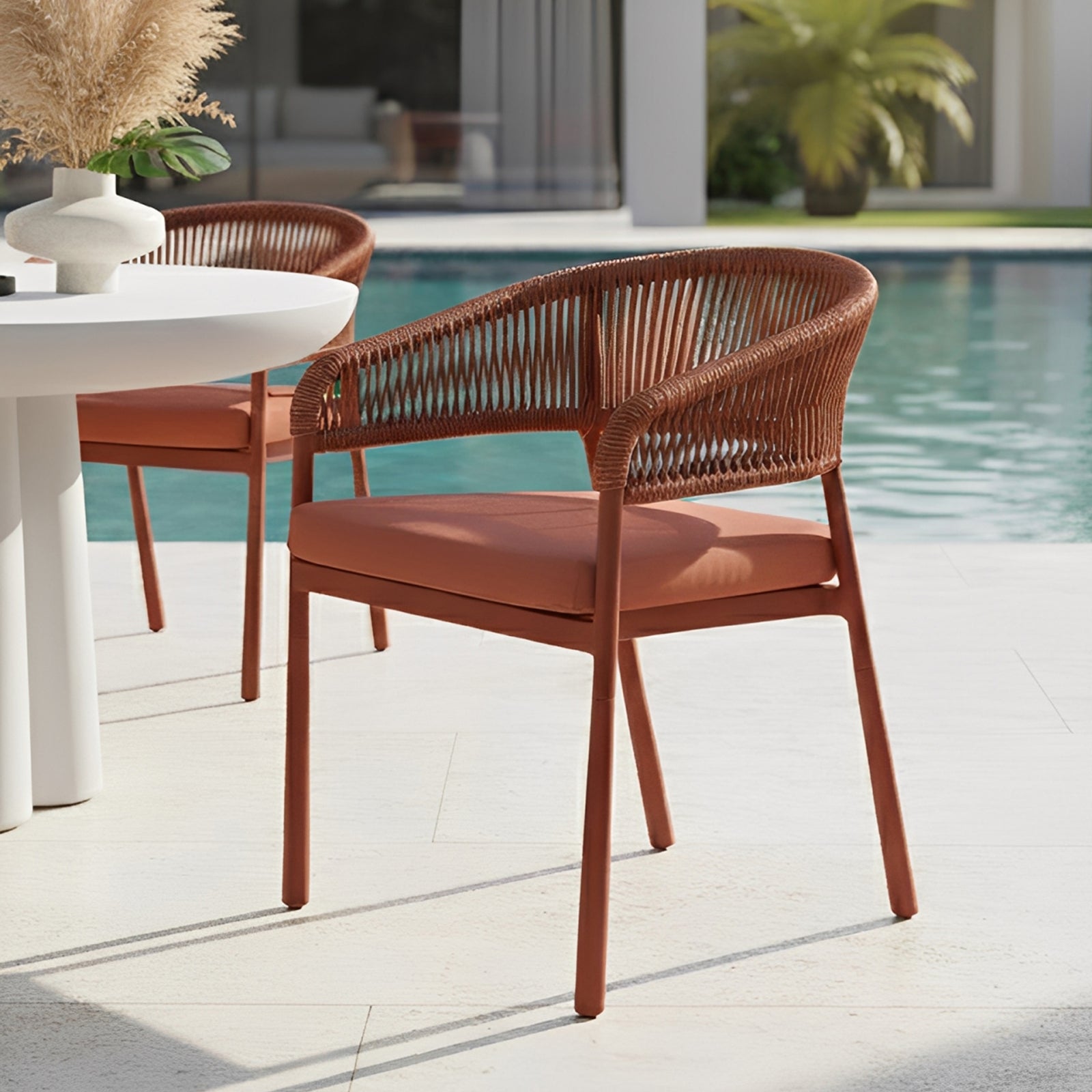 Coastal Outdoor Rope Dining Chairs Set of 2 in Burnt Orange by a sunlit pool, featuring rust-colored, rope-woven design with a sturdy frame and cushioned seats, enhancing a stylish alfresco setting.