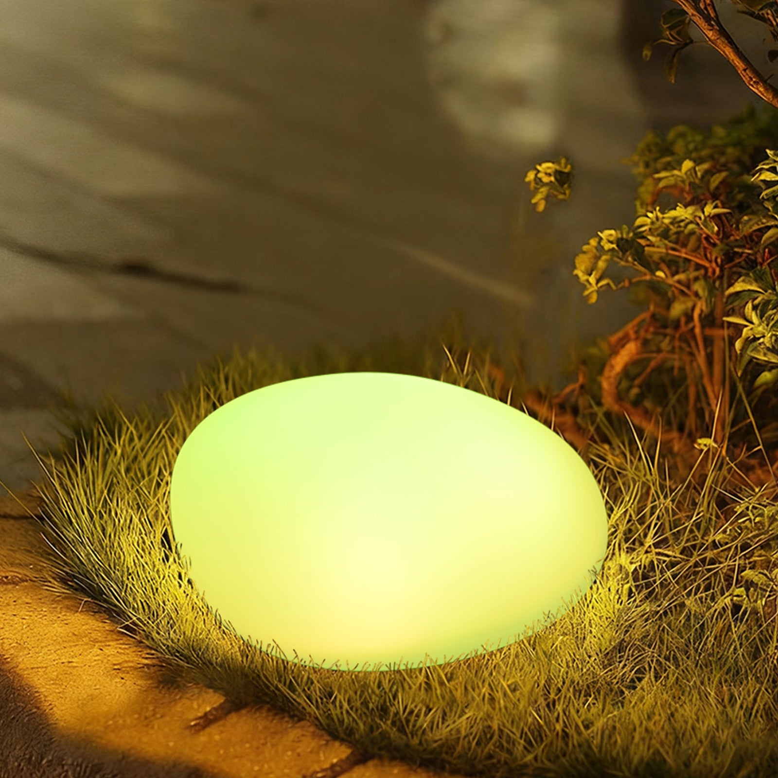Solar Outdoor LED Rock Light Waterproof Garden Lamp glowing greenish-yellow, pebble-shaped, on grass beside a garden path, enhancing outdoor ambiance with its smooth, natural stone appearance and soft illumination.