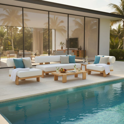 Modica 5 Seater Aluminium Outdoor Sofa Set in White on sunlit pool deck, featuring low-profile seating with white cushions, blue and gray pillows, and a matching coffee table with fruit bowl and water glasses.