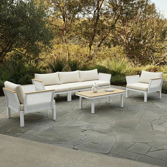 Sierra Outdoor Lounge Set in Beige features a three-seat sofa, two armchairs with off-white cushions, and a coffee table with a white base and wood-tone slats on a garden patio.