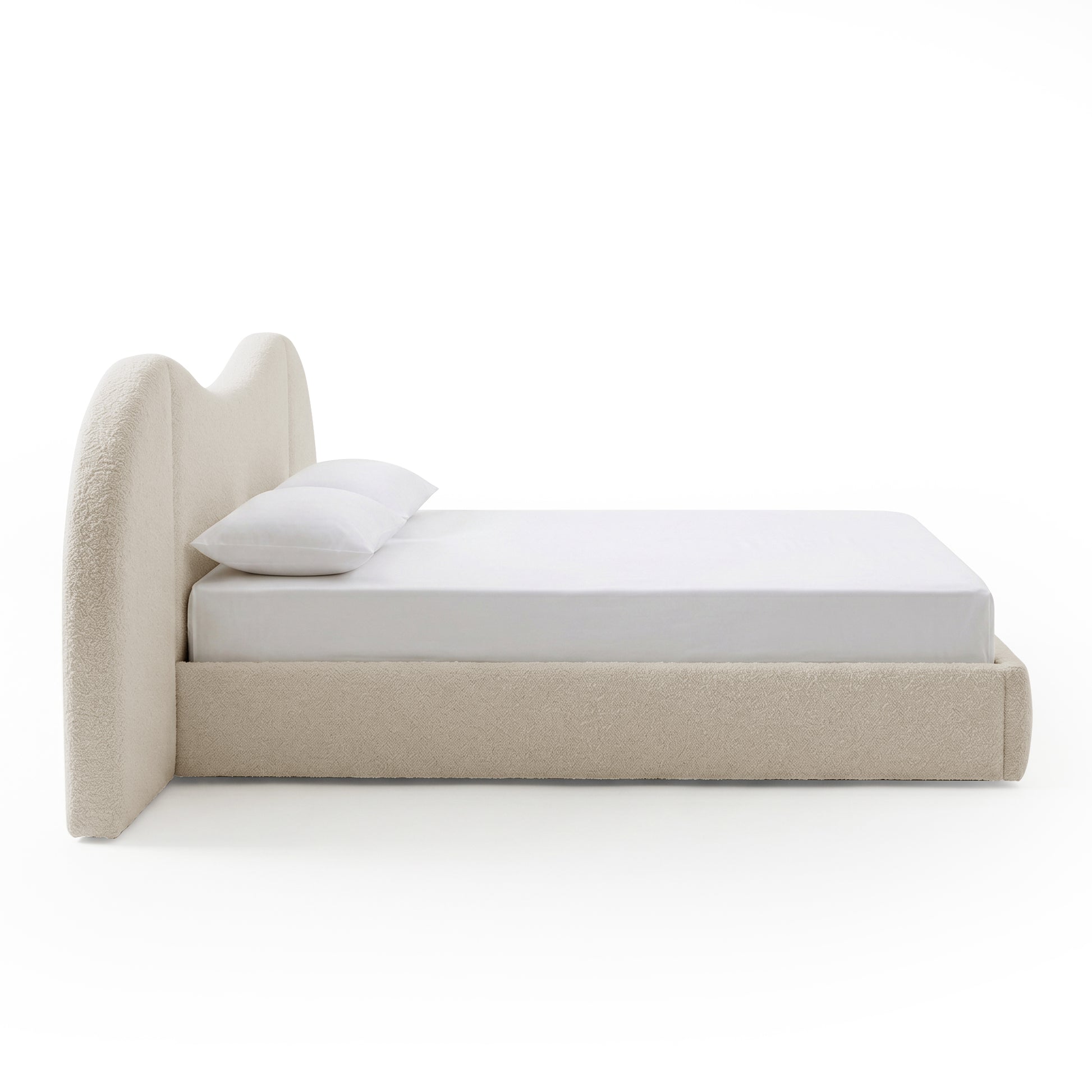 Side view of upholstered bed with white bedding on white background