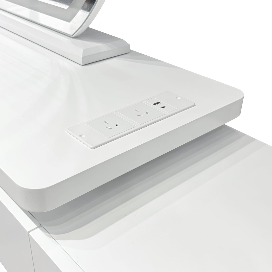 Close-up of the Alora LED Mirror Makeup Vanity Table with Storage in White, featuring a built-in power module with two three-pin outlets and a USB port, visible near the monitor stand base.