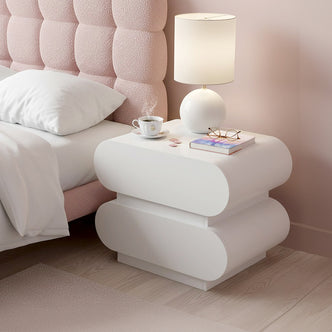 Ardenne 55cm Curved Bedside Table with Drawers in White, featuring a sleek double-rounded design, topped with a lamp, coffee, book, and eyeglasses, beside a blush-pink quilted headboard.