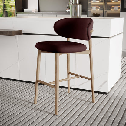 Audrey Fabric Upholstered Barstool Set of 2 in Dark Plum, featuring light wooden legs, rounded padded seat, and curved backrest, positioned in a modern kitchen with a marble-style island and grey rug.