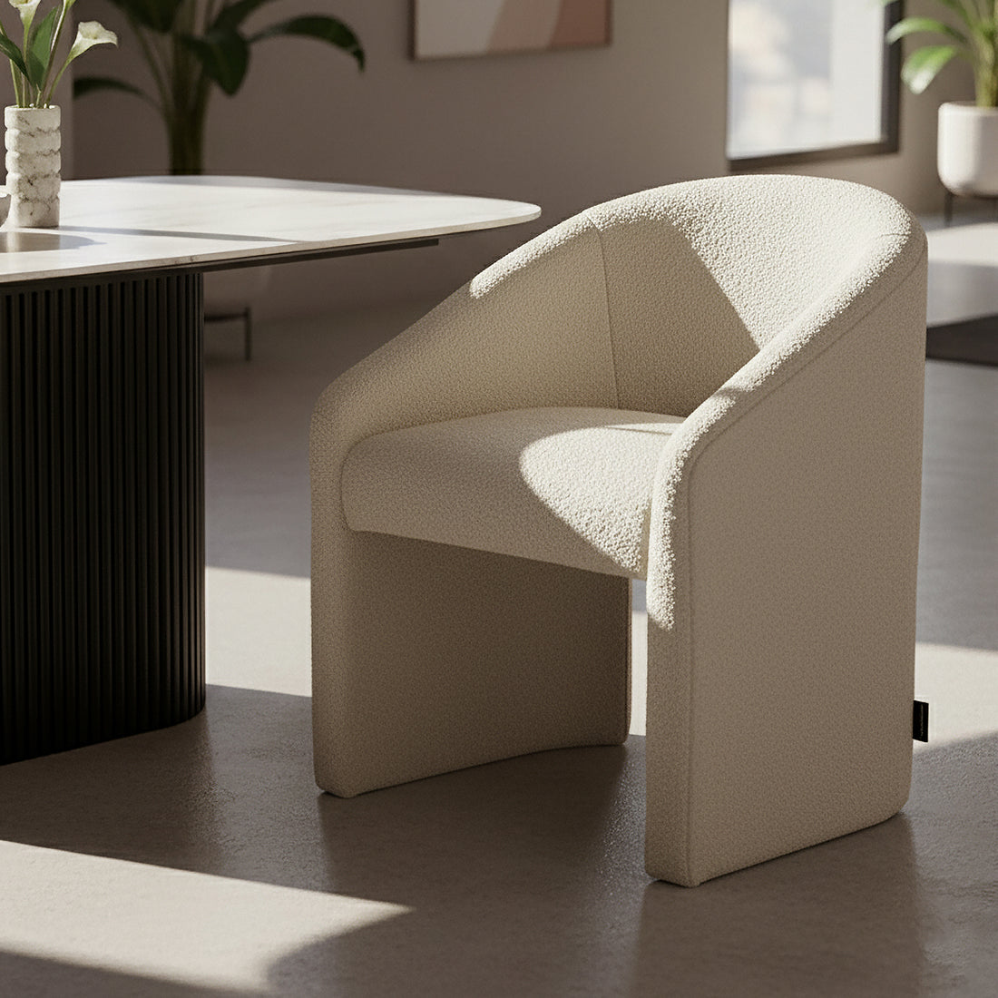 Nuve Bouclé Upholstered Accent Armchair in Cream White, featuring a curved back and soft boucle fabric, placed in a minimalist corner with natural light, near a fluted pedestal table with calla lilies.