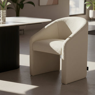 Nuve Bouclé Upholstered Accent Armchair in Cream White, featuring a curved back and soft boucle fabric, placed in a minimalist corner with natural light, near a fluted pedestal table with calla lilies.