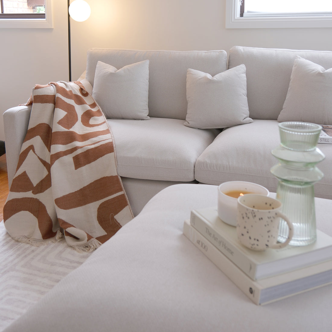 Light beige sofa in a styled living room with pillows, blanket, and ottoman