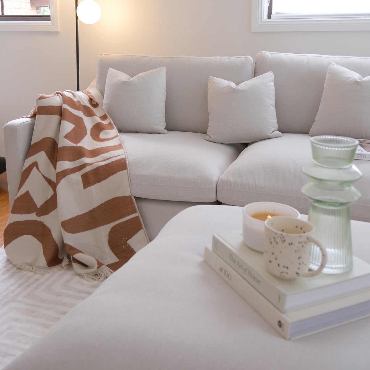 Light beige sofa in a styled living room with pillows, blanket, and ottoman