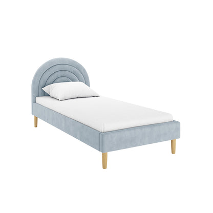 Estilla Velvet Rainbow Bed in Ice Blue, featuring a light blue upholstered frame with a rounded, tufted headboard, on natural-wood legs. The bed is dressed in a plain white sheet and pillow.