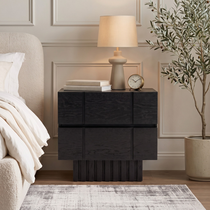 Black nightstand styled in a bedroom next to a bed with decor items