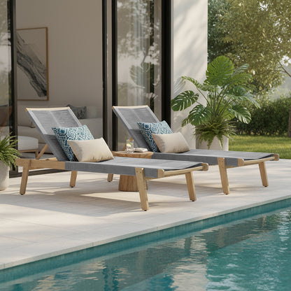 Aureli Hardwood Acacia Reclining Sun Lounger in Light Grey with teak-toned frame, gray woven sling seat, and decorative pillows, beside a round side table on a poolside terrace.