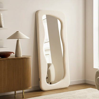 Sabrina 180cm Curved Full Length Mirror in Beige features a padded, undulating frame against a pale wall, enhancing a minimalist living room corner with a serene, contemporary feel.