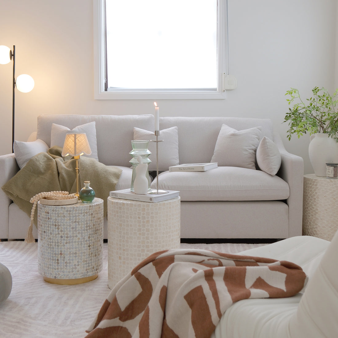 Light grey or beige sofa styled in a bright modern living room with side tables and decor