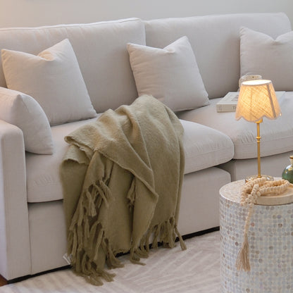 Close-up section of a light-colored sectional sofa with pillows and a throw blanket in a styled room