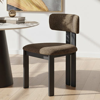 Haleo Curved Boucle Dining Chair Set of 2 features a rounded back and thick upholstered seat on a sleek black metal frame, positioned beside a marble-topped round table with decorative items.