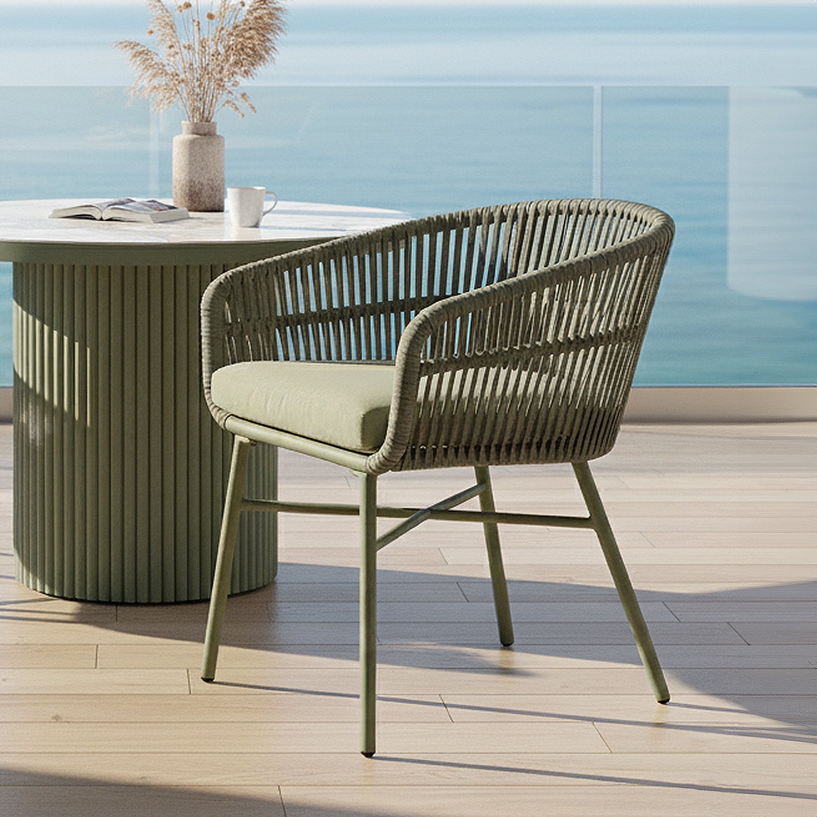 Marula Rope Outdoor Dining Chairs in Green Set of 4, featuring a powder-green metal frame and woven rope design, create a relaxed seaside patio vibe with a matching green fluted side table.