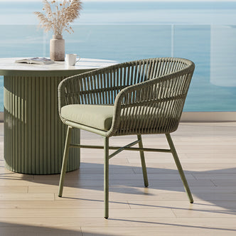 Marula Rope Outdoor Dining Chairs in Green Set of 4, featuring a powder-green metal frame and woven rope design, create a relaxed seaside patio vibe with a matching green fluted side table.