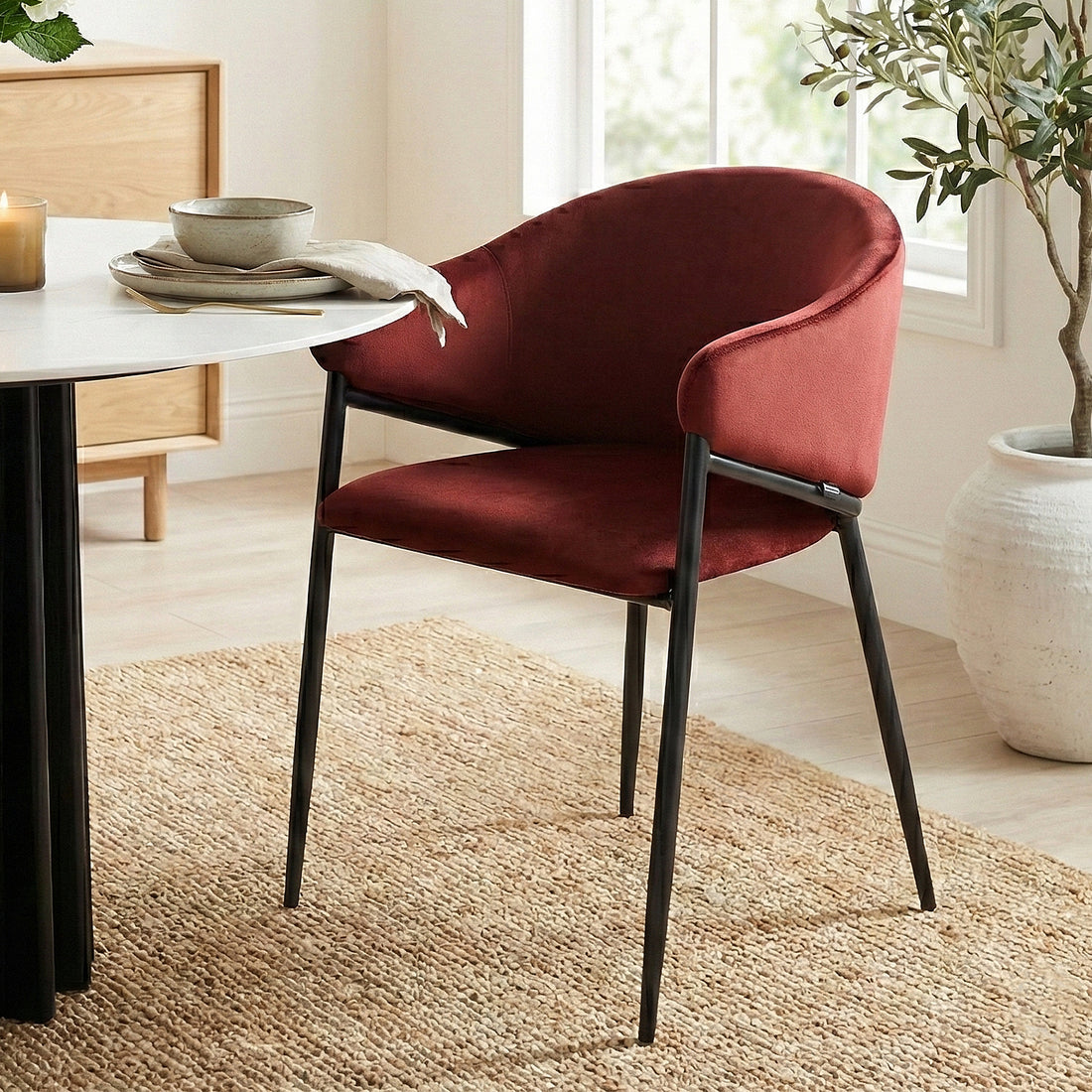 Burgundy velvet chair at a white dining table on a woven rug in a bright room