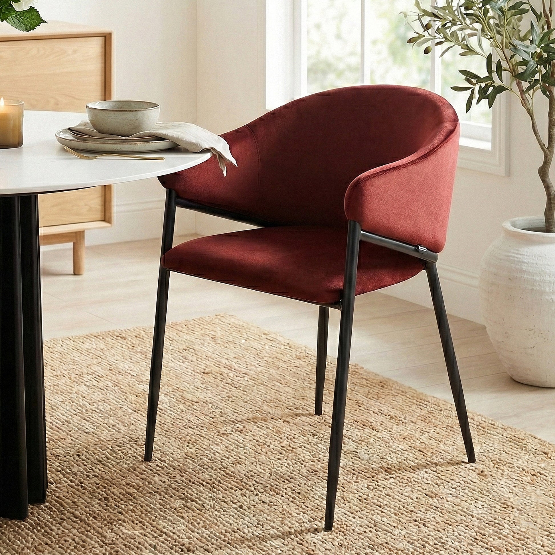 Burgundy velvet chair at a white dining table on a woven rug in a bright room