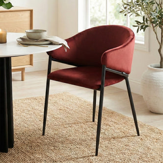 Burgundy velvet chair at a white dining table on a woven rug in a bright room