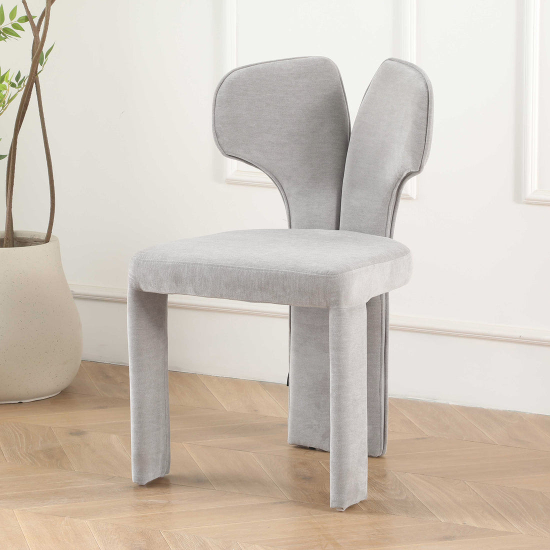 Light gray chair in living space with wood flooring and potted plant