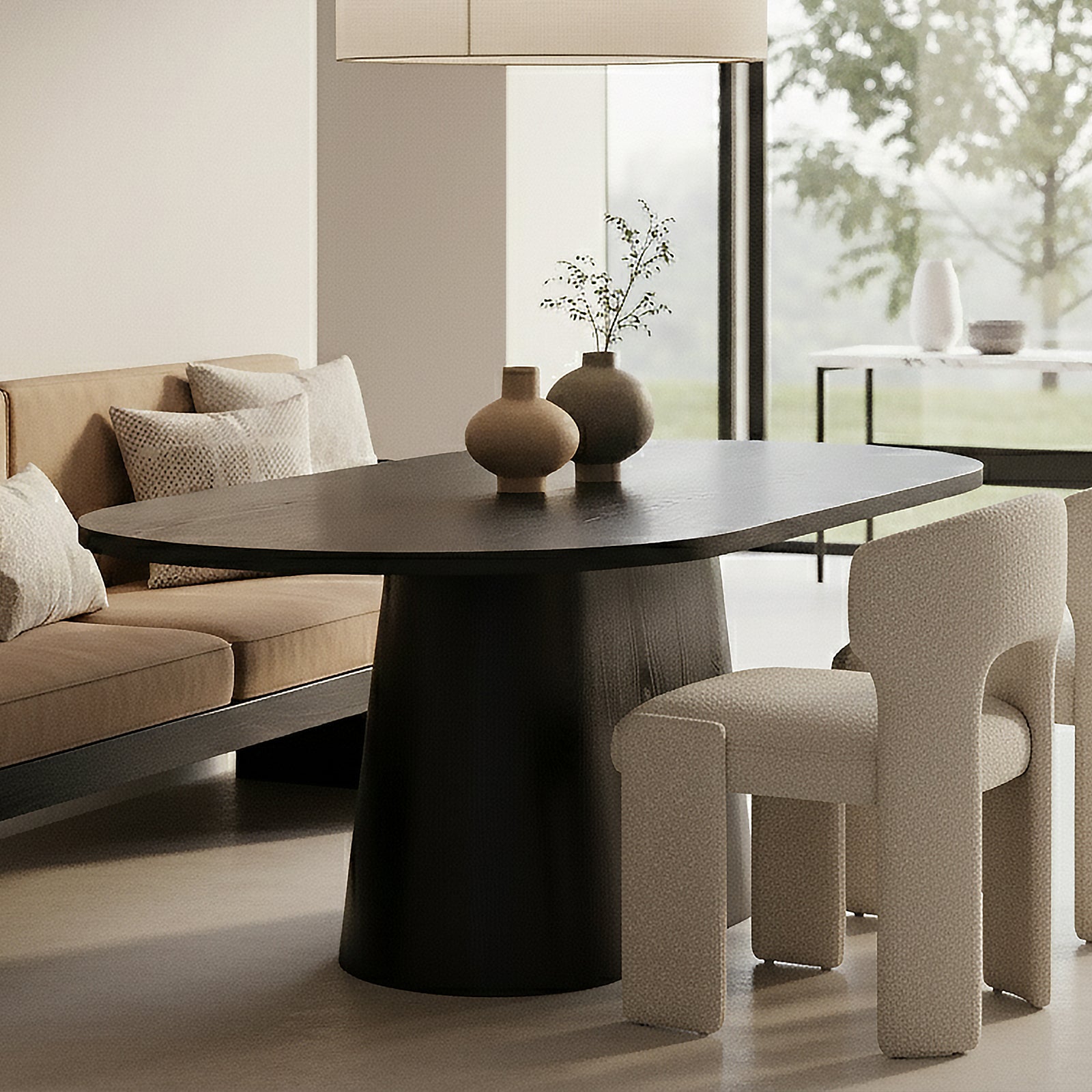 Gigi 180cm Oval Wooden Dining Table in Black with pedestal base, two ceramic vases with greenery, placed in a minimalist dining area with taupe sofa and upholstered off-white chair.