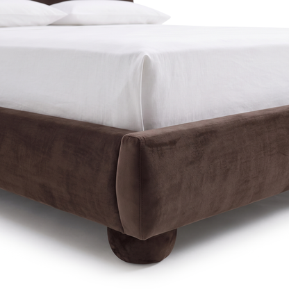 Close-up of the lower corner of a dark brown upholstered bed frame on white background