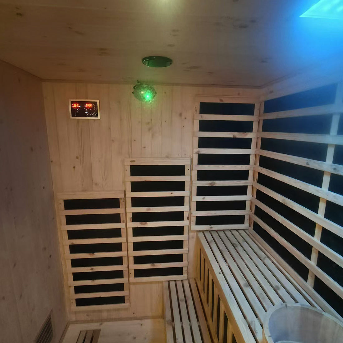 Interior of the Luxo Kiima 6 Person Hybrid Finnish Outdoor Sauna in Natural, featuring cedar paneling, infrared heater panels, a wooden bench, digital control module, and a wooden bucket.