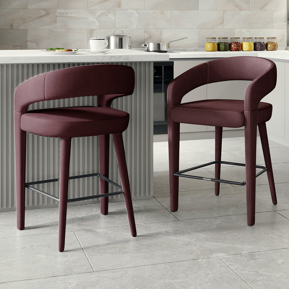 Eisha Velvet Bar Stool Set of 2 in Dark Plum features upholstered stools with rounded backs, padded seats, and slim wooden legs with metal footrests, complementing a contemporary kitchen or breakfast bar setting.