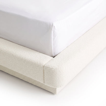 Close-up corner view of an upholstered bed with white bedding on a white background