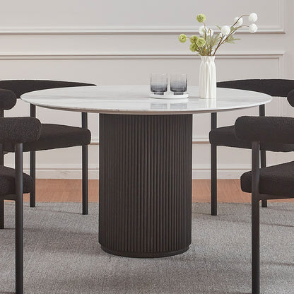 Gracie 120cm Round Marble Dining Table in Black features a white marble top on a black fluted base, surrounded by four plush black chairs, complemented by a vase and glasses on top.