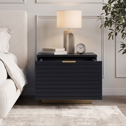 Black nightstand styled in a bedroom next to a bed with lamp, books, and decor