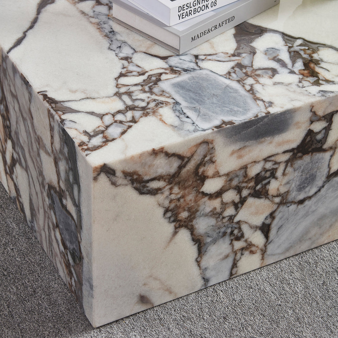 The Solene 100cm Coffee Table in Blue Galaxy features a white marble surface with striking brown and gray veining, topped with hardcover books, set on a low-pile grey carpet.