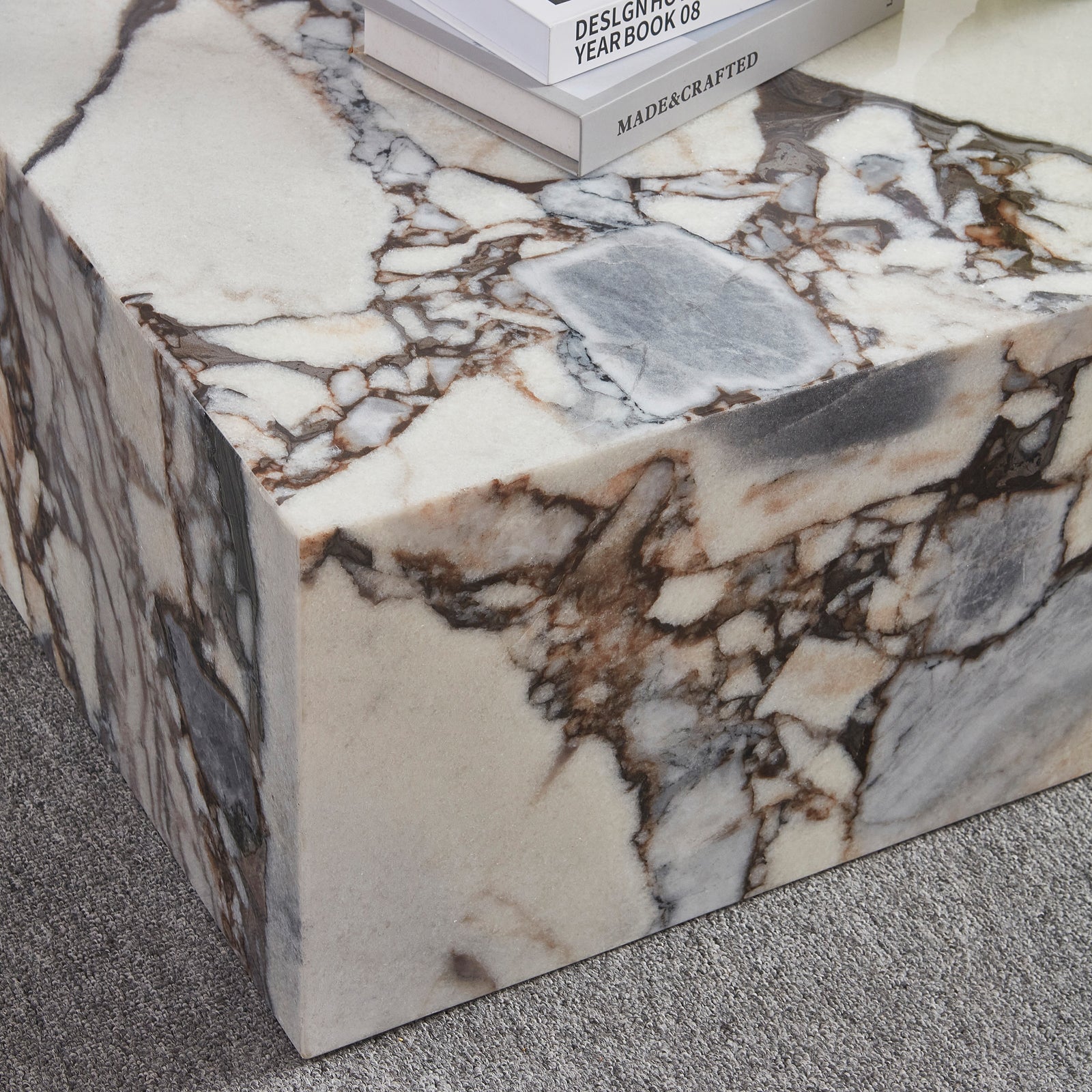 The Solene 100cm Coffee Table in Blue Galaxy features a white marble surface with striking brown and gray veining, topped with hardcover books, set on a low-pile grey carpet.