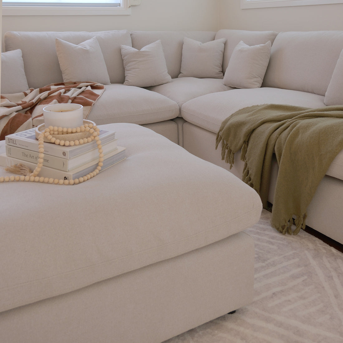 Light-colored sectional sofa with ottoman in a warm living room setting