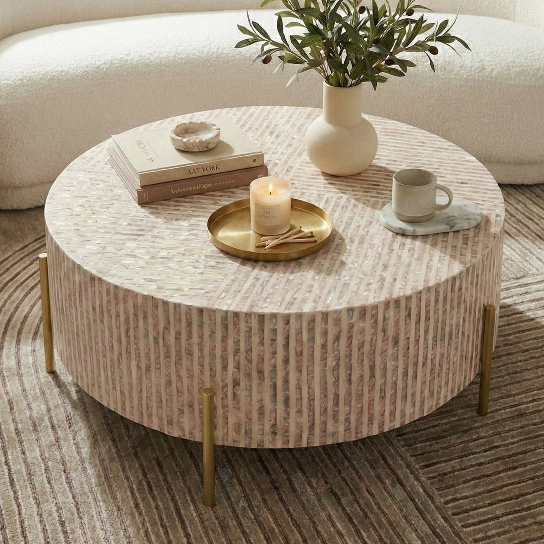 Round coffee table on patterned rug in front of curved sofa, styled with books, candle, tray, and greenery