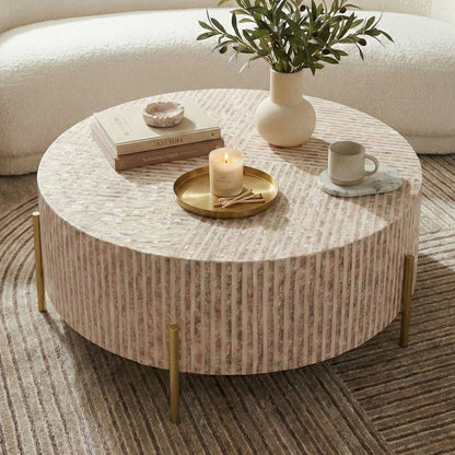 Round coffee table on patterned rug in front of curved sofa, styled with books, candle, tray, and greenery