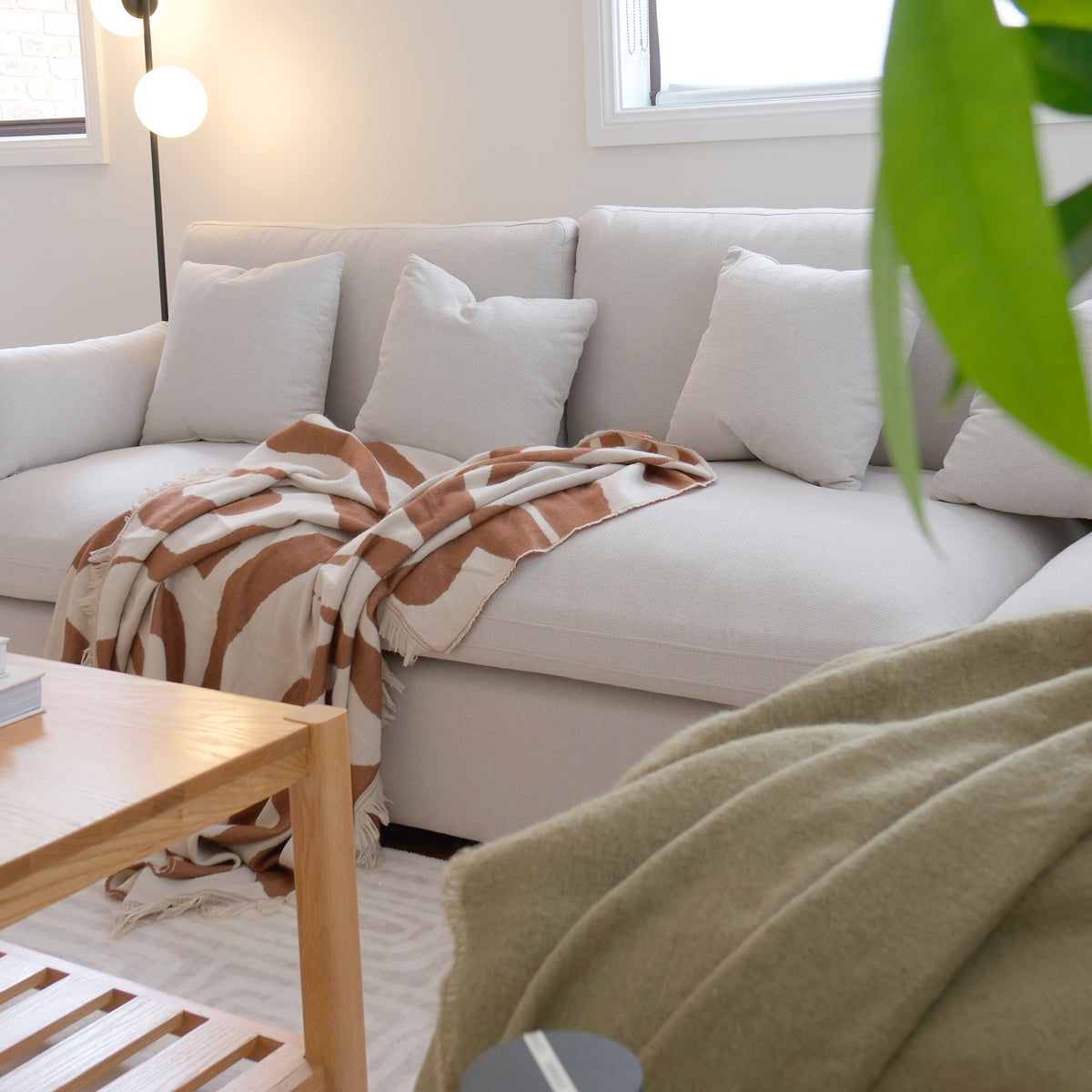 Light-colored sectional sofa in a bright living room with blanket and pillows.