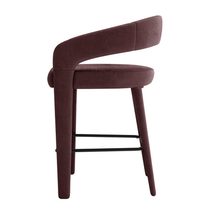 Eisha Velvet Bar Stool Set of 2 in Dark Plum features a side-view of a bar-height stool with a curved backrest, plum velvet upholstery, round seat, splayed legs, and integrated black metal footrest.