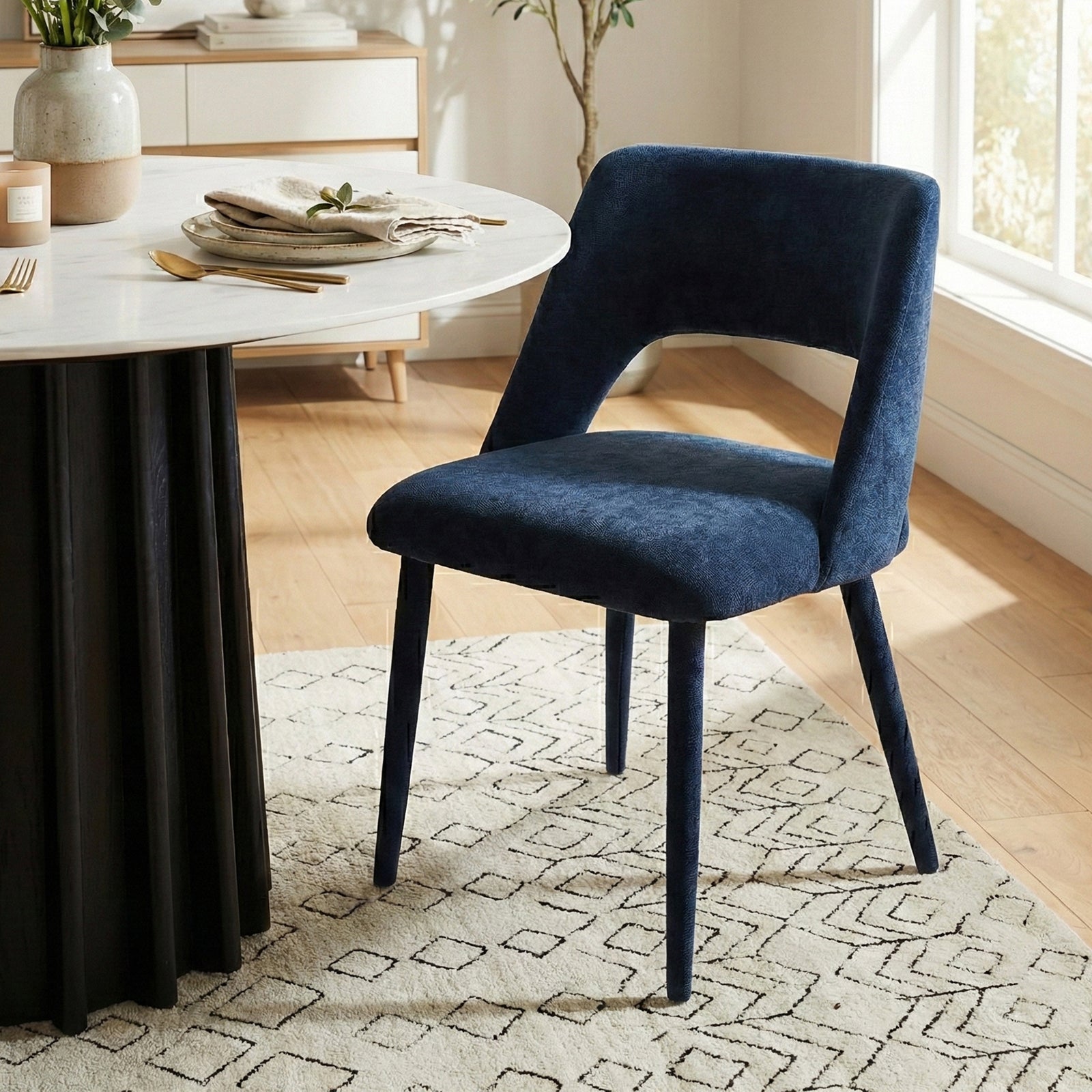 Dark blue velvet chair beside a round dining table in a modern, well-decorated room with plants and accessories