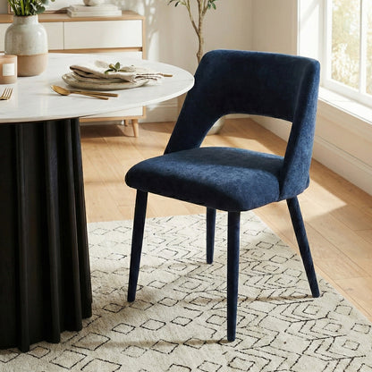 Dark blue velvet chair beside a round dining table in a modern, well-decorated room with plants and accessories