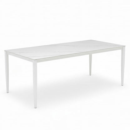 Cabria 7 Piece Sintered Stone Outdoor Dining Set in Beige, featuring a sleek rectangular table with a white marble-patterned top and slim, tapered legs, complemented by six cushioned dining chairs.