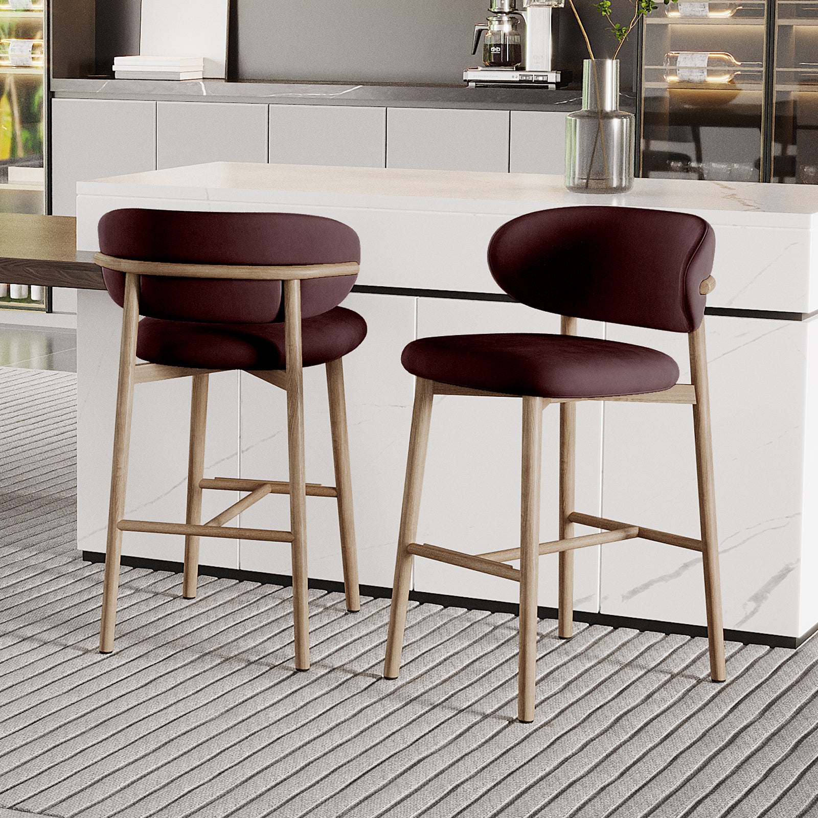 Audrey Fabric Upholstered Barstool Set of 2 in Dark Plum, featuring backless design, light wood legs, and plush seats. Positioned at a white marble-effect counter with a coffee machine and vase on top.
