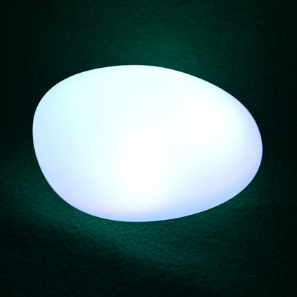 Solar Outdoor LED Rock Light Waterproof Garden Lamp emits a cool white glow on a dark surface, resembling a natural stone. Ideal for gardens with its smooth, egg-shaped design and cordless operation.